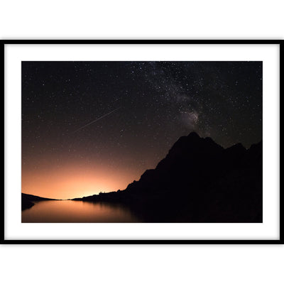 Een ingelijste poster met een sterrenhemel met een gouden zonsondergang met op de voorgrond donkere bergen.